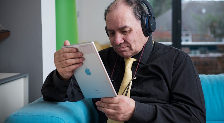 A man wearing headphones and using his iPad to listen to RNIB Talking Books.