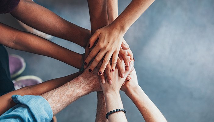 Several people holding their hands in a group circle in solidarity with each other.