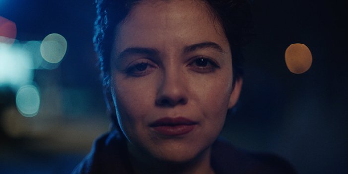 Ava's face close up at night outside, lit up by the street lights.