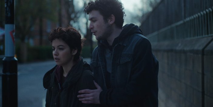 Girl and boy on the side of a street by a lamp post with a grey sky setting