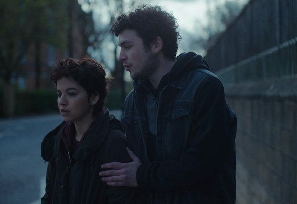 Girl and boy on the side of a street by a lamp post with a grey sky setting