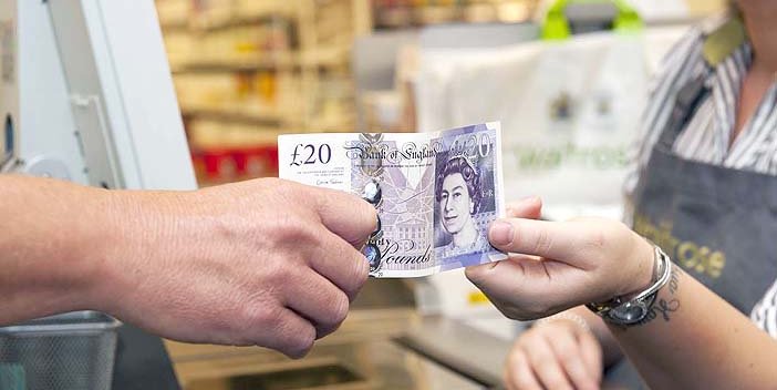 A man handing a twenty pound note to a member of staff in a supermarket.