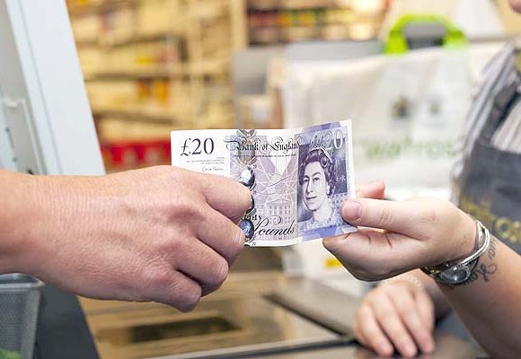 A man handing a twenty pound note to a member of staff in a supermarket.