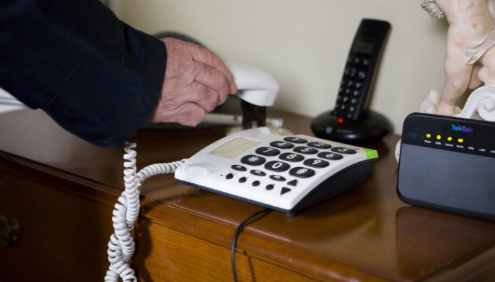 Hands of an older man replacing the receiver on a large-buttoned telephone