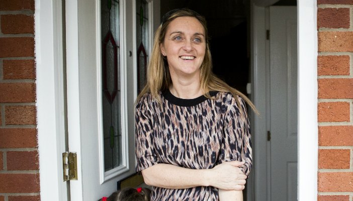 Smiling young woman standing in the doorway of her home