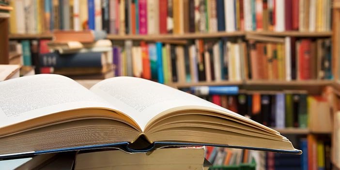 A book lays open on a stack of books in a library.
