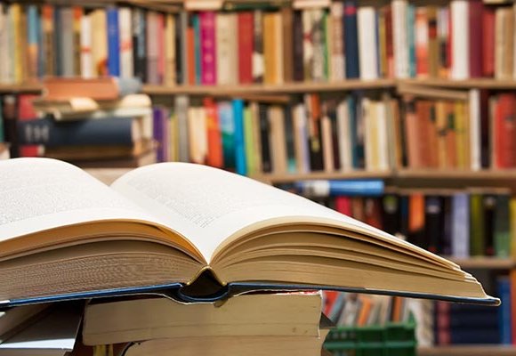 A book lays open on a stack of books in a library.
