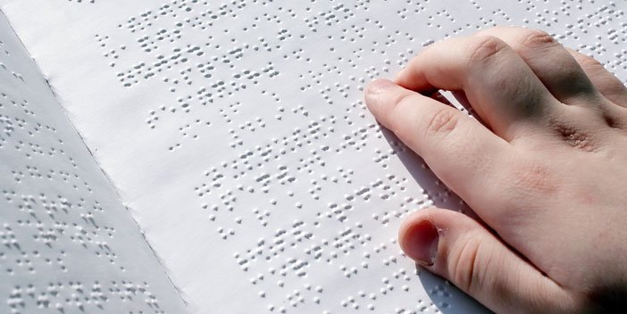 A closeup of a person’s hand as they read a braille book. Their hand is tracing along a sentence in the middle of the page.