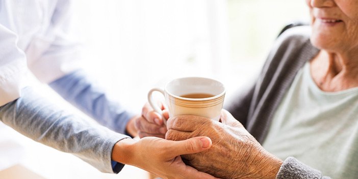 A carer handing a cup of tea to an older person.
