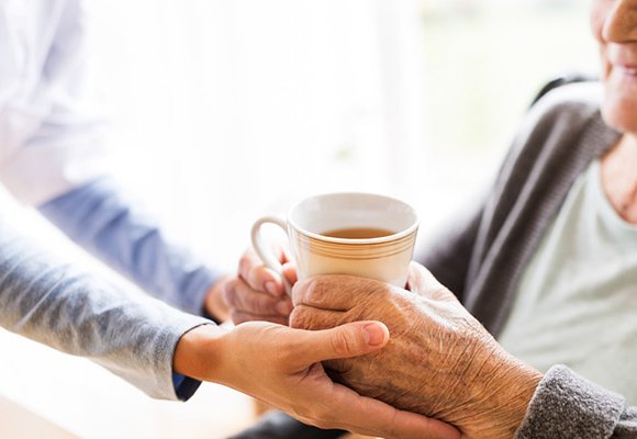 A carer handing a cup of tea to an older person.