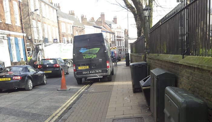 A large van parked on the pavement, blocking most of the path for pedestrians.