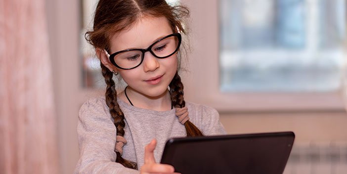 A young girl wearing glasses uses a tablet computer