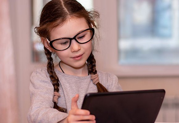 A young girl wearing glasses uses a tablet computer