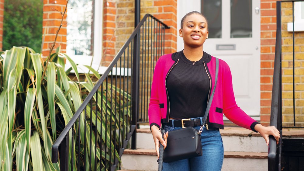 A young woman walking down the steps outside her front door using a cane and smiling.