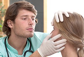 A health care professional wearing gloves and examining a young woman’s eyes.