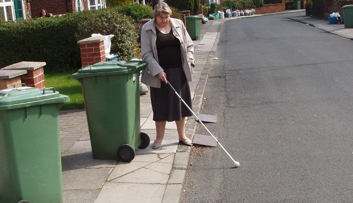 Judith trying to navigate around poorly placed wheelie bins with her white cane.