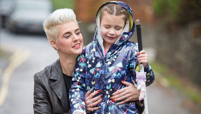 A young girl who is blind and holding a cane. Being supported by her mother.