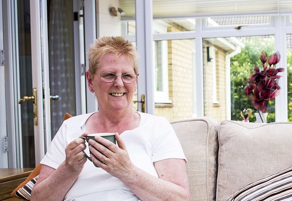 Lady sat on a sofa in a conservatory enjoying a cup of tea.