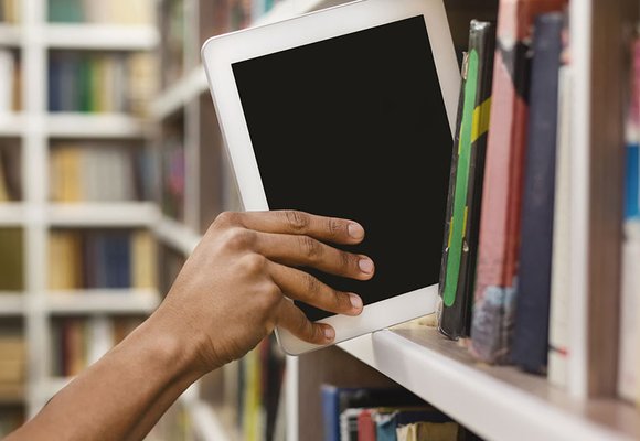 A person taking a tablet off a shelf filled with books.