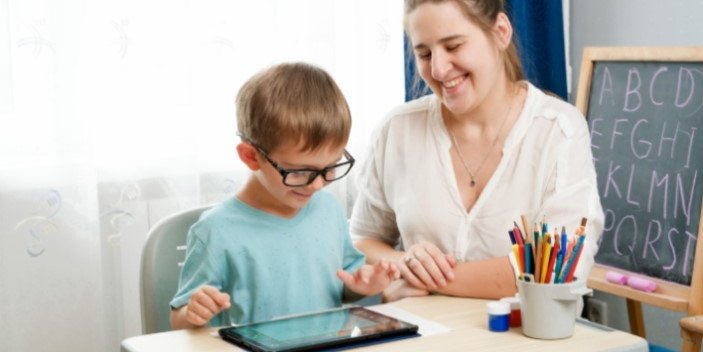 A young boy sitting at a desk being taught by an adult.