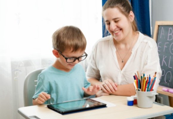 A young boy sitting at a desk being taught by an adult.