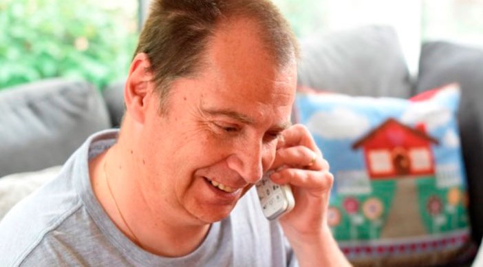 A man smiling and talking on the phone in his home.