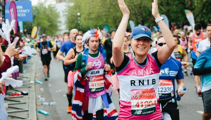Hundreds of runners at the Oxford Half Marathon. Anna, a runner in a pink RNIB shirt, has her arms raised in celebration.
