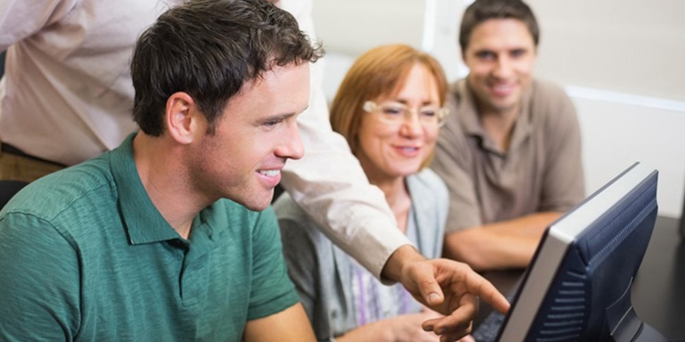 A group gathered round a computer as a trainer points out something to them on the screen.