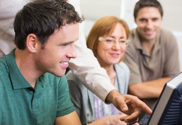 A group gathered round a computer as a trainer points out something to them on the screen.