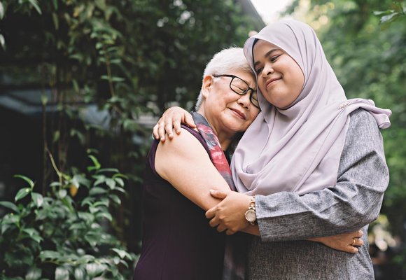 Two women in a caring embrace standing in front of lush vegetation