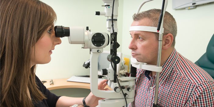 An optician examining a man's eyes with a slit lamp.