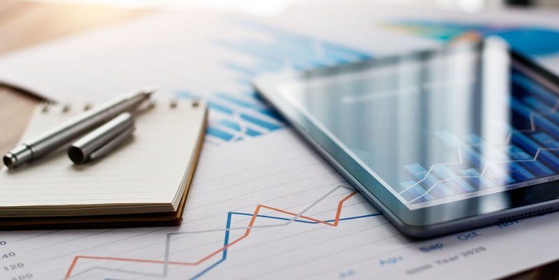 A close-up image of a statistic report with a few papers and a computer tablet on top of a spreadsheet.