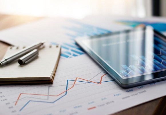 A close-up image of a statistic report with a few papers and a computer tablet on top of a spreadsheet.