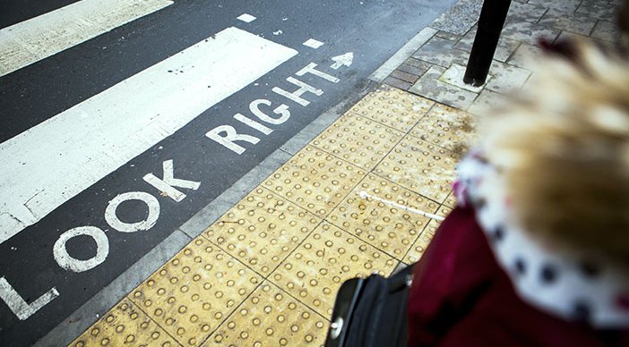 A pedestrian walking to a zebra crossing with tactile paving. There is a sign saying ‘look right’ with an arrow pointing to the right painted on the ground.