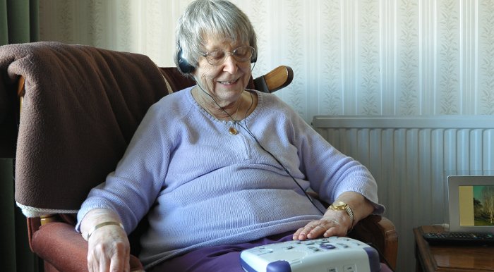 A woman sits in a chair and listens to a talking book.