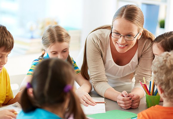 A teacher interacting a group of children as they draw in workbooks.