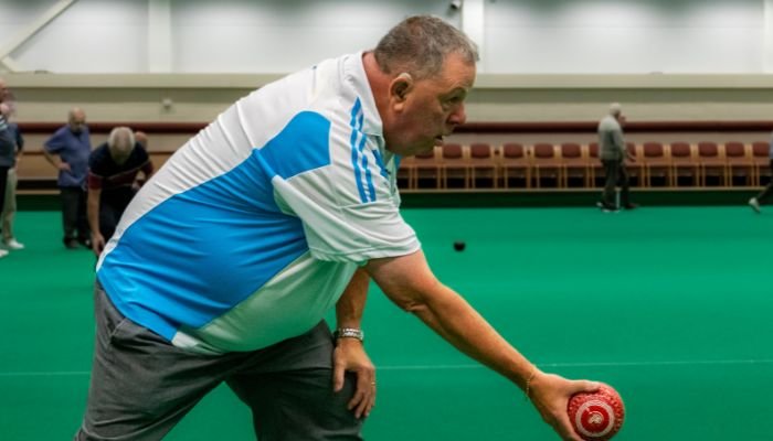 Side view of a man in a white and blue polo shirt playing indoor bowls.