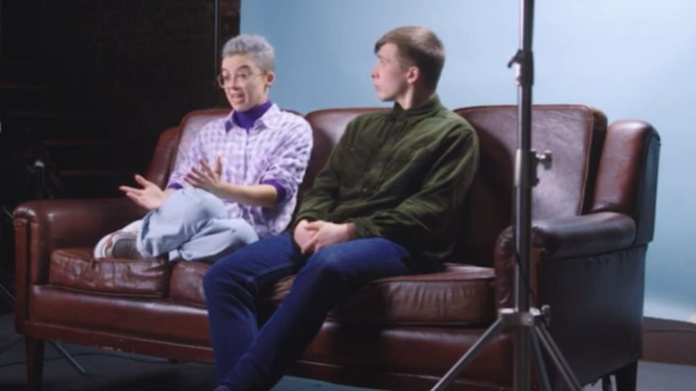 Two people sit talking on a leather sofa.
