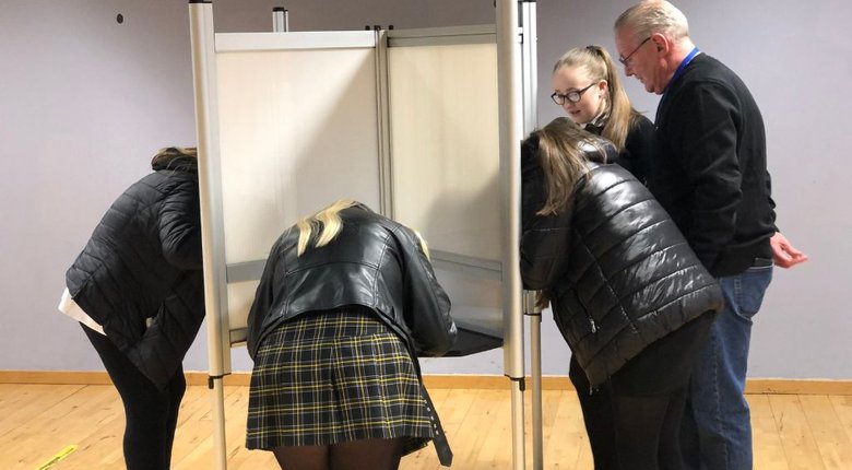 School pupils stand in private voting booths writing their vote down.
