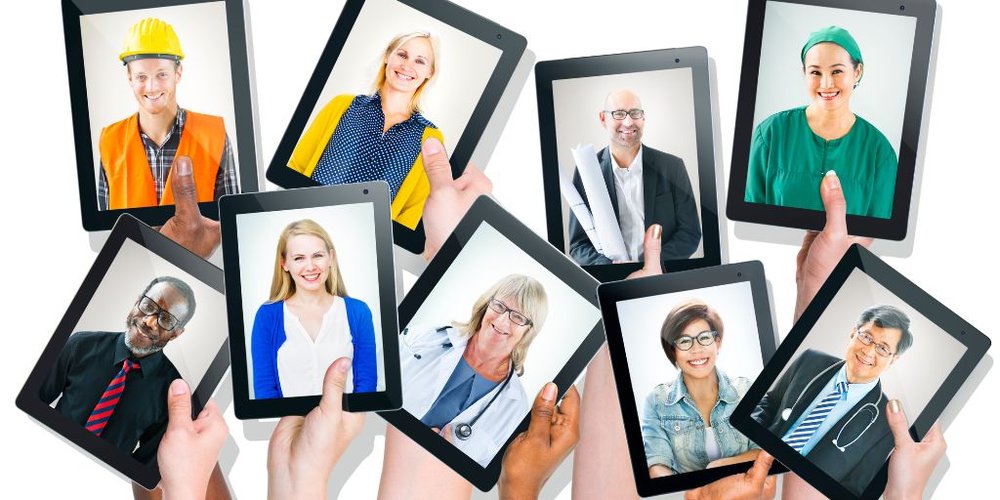 Hands hold up nine electronic tablets against a white background. Each tablet displays an image of someone wearing a work uniform.