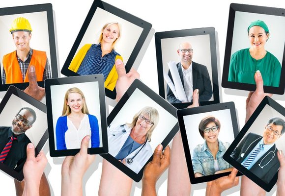 Hands hold up nine electronic tablets against a white background. Each tablet displays an image of someone wearing a work uniform.