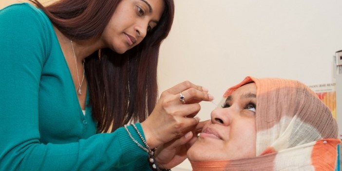 A woman having eye drops put in their eye by a eye care professional.