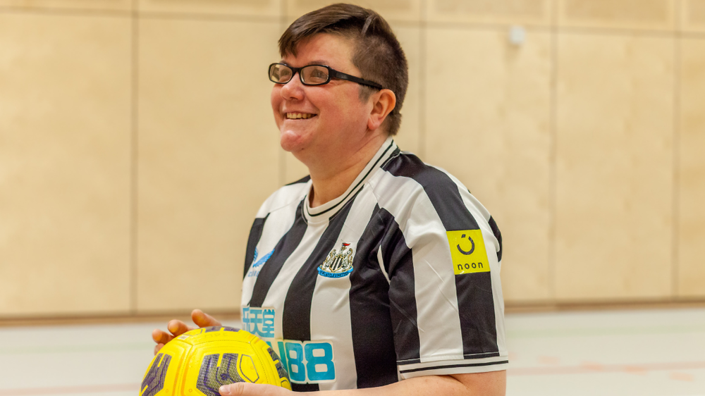 A woman holding a football and smiling in a sports hall