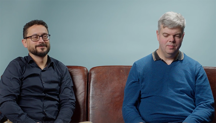 Two men sitting next to each other on a sofa.