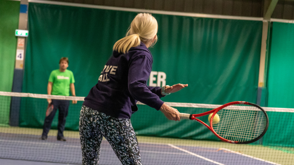 A man and a woman playing tennis in an indoor court.