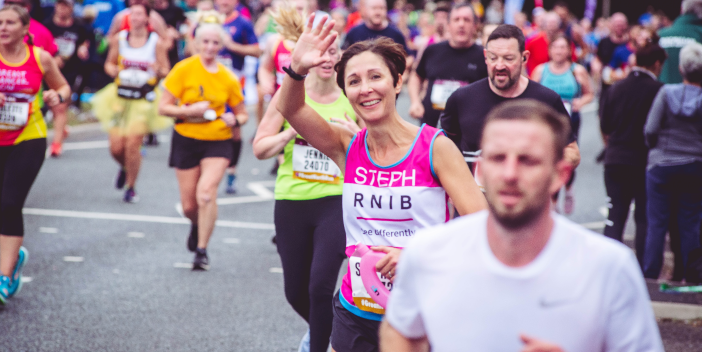 A large group of runners. One is wearing a pink RNIB shirt and waving to the camera.