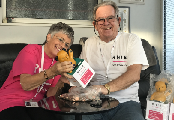 RNIB volunteers Alan and Janet on a sofa, smiling and counting donations from Sooty Boxes.