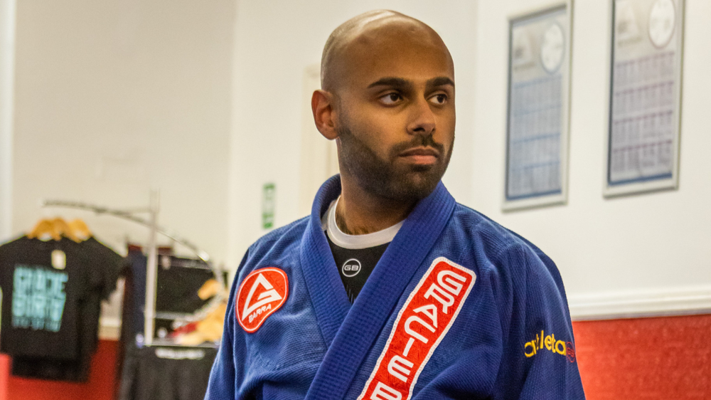 A man knelt on the floor, in his jiu-jitsu uniform
